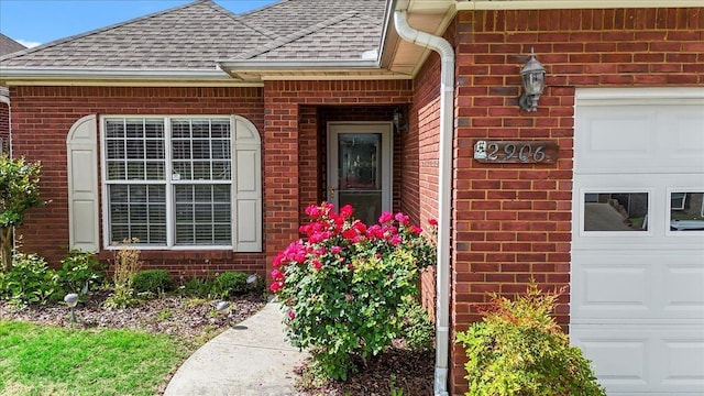 entrance to property with roof with shingles, brick siding, and a garage