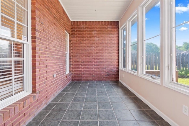 unfurnished sunroom with brick wall, baseboards, and tile patterned flooring
