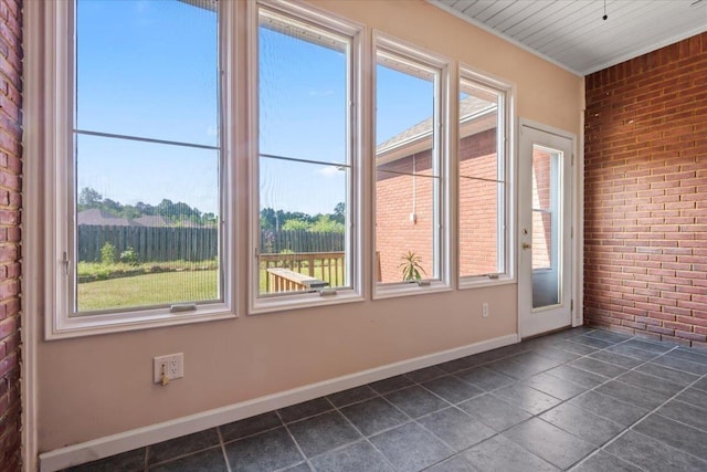 empty room featuring brick wall, dark tile patterned flooring, baseboards, and crown molding