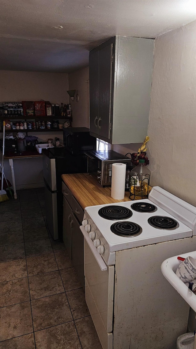 kitchen featuring a textured ceiling, white electric range, stainless steel fridge, and dark tile patterned flooring