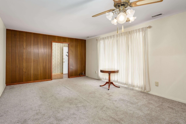 carpeted empty room with ceiling fan and wooden walls