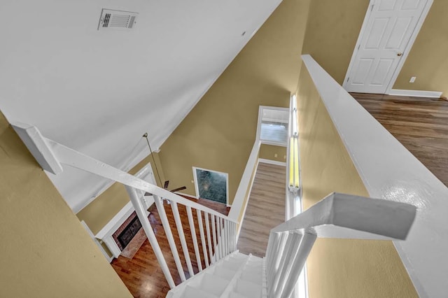 stairs featuring hardwood / wood-style flooring, high vaulted ceiling, and a brick fireplace