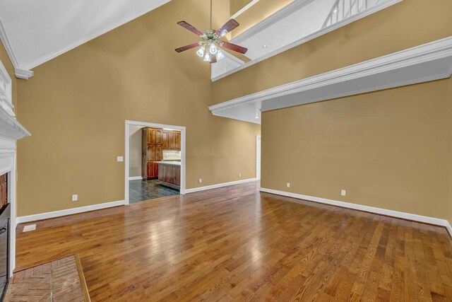 unfurnished living room featuring ceiling fan, a high ceiling, crown molding, hardwood / wood-style floors, and a fireplace