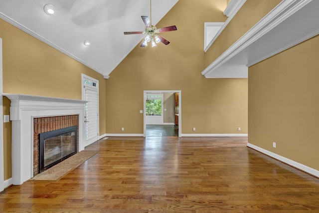 unfurnished living room with a high ceiling, a brick fireplace, hardwood / wood-style flooring, ceiling fan, and ornamental molding