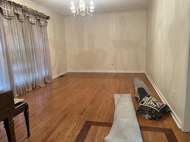 empty room featuring hardwood / wood-style flooring, ornamental molding, a textured ceiling, and an inviting chandelier