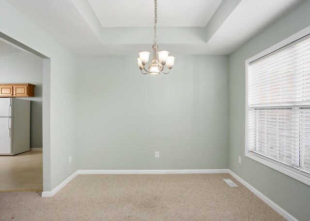 carpeted spare room with a raised ceiling and a chandelier