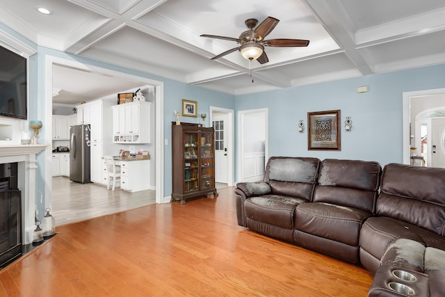 living area with a fireplace, light wood-style flooring, a ceiling fan, coffered ceiling, and beamed ceiling