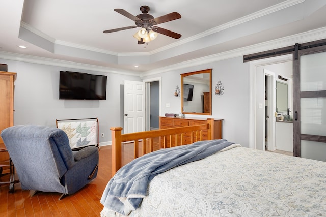 bedroom with a barn door, a raised ceiling, ornamental molding, wood finished floors, and recessed lighting