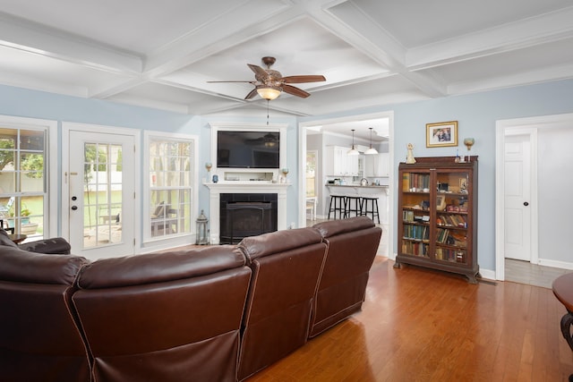 living area with beamed ceiling, coffered ceiling, a tiled fireplace, and wood finished floors