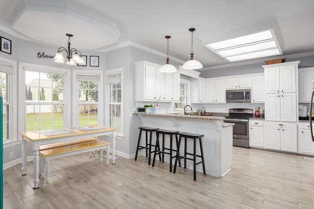 kitchen with a breakfast bar area, stainless steel appliances, a peninsula, white cabinetry, and ornamental molding