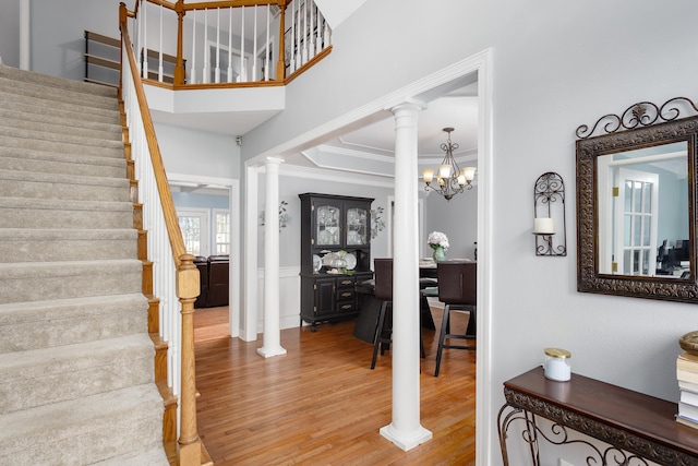 foyer entrance featuring stairway, wood finished floors, crown molding, ornate columns, and a chandelier