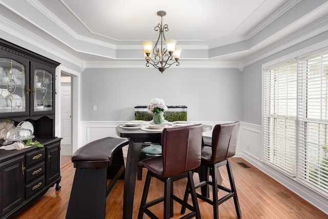 dining space featuring a raised ceiling, visible vents, wood-type flooring, an inviting chandelier, and wainscoting