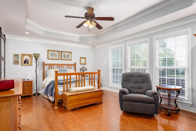 bedroom with a barn door, light wood-style flooring, baseboards, a tray ceiling, and crown molding