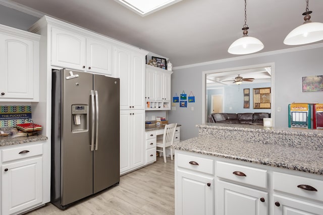 kitchen featuring light stone counters, stainless steel fridge, crown molding, and white cabinetry