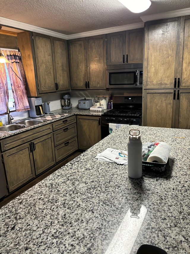 kitchen with light stone counters, black range with gas stovetop, dark brown cabinets, and a textured ceiling