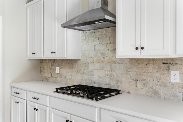 kitchen with stainless steel gas cooktop, wall chimney range hood, white cabinets, and backsplash