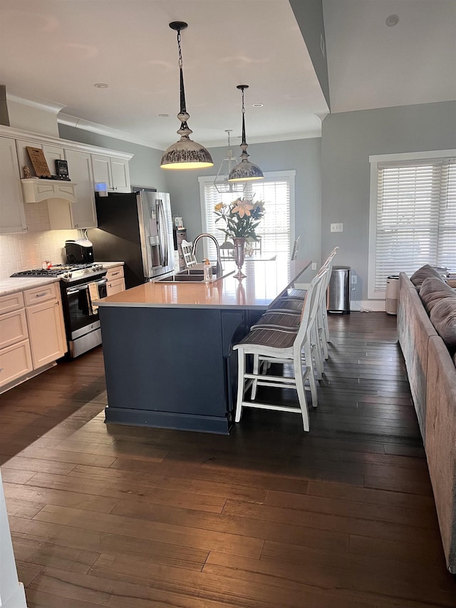 kitchen featuring decorative light fixtures, appliances with stainless steel finishes, a center island with sink, and white cabinets