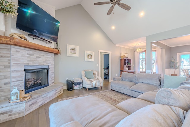 living area featuring high vaulted ceiling, a fireplace, wood finished floors, a ceiling fan, and crown molding