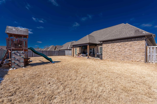 exterior space with a playground, brick siding, a fenced backyard, and roof with shingles