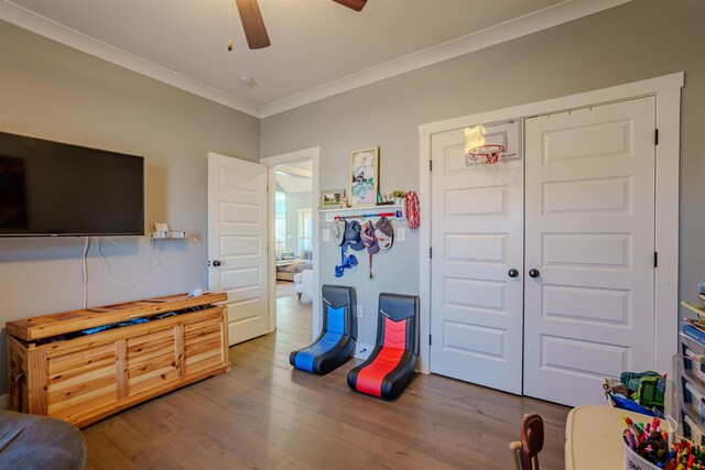 rec room with a ceiling fan, ornamental molding, and wood finished floors