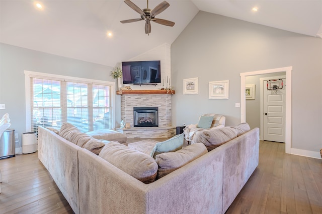 living room featuring high vaulted ceiling, light wood finished floors, a fireplace, and a ceiling fan