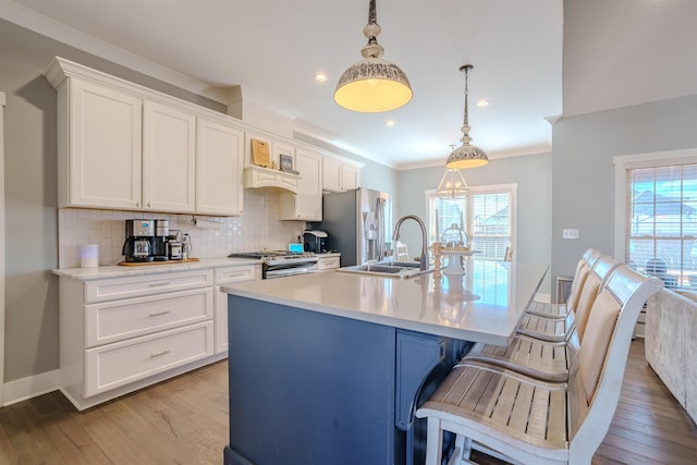 kitchen with a center island with sink, appliances with stainless steel finishes, hanging light fixtures, light countertops, and a sink