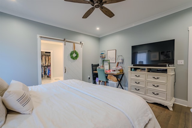 bedroom featuring a barn door, ceiling fan, ornamental molding, dark wood-type flooring, and a spacious closet