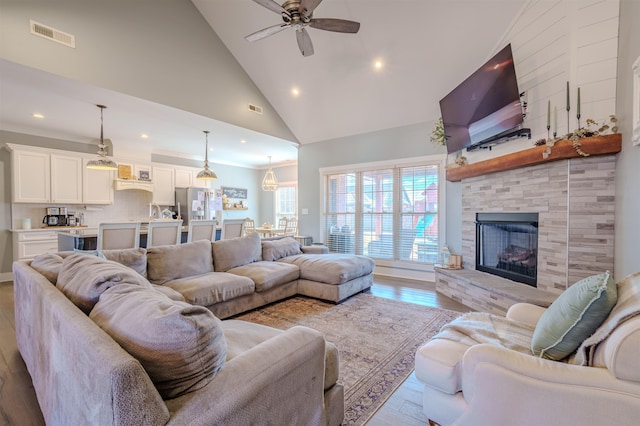 living room with light wood finished floors, visible vents, a ceiling fan, a stone fireplace, and high vaulted ceiling