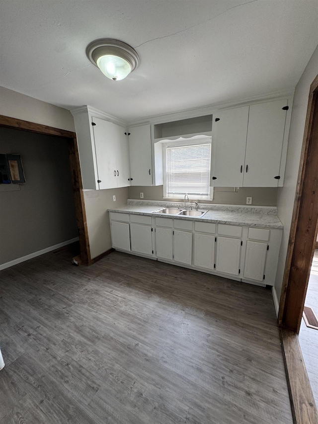 - kitchen with a sink, white cabinets, wood finished floors, light countertops, and baseboards