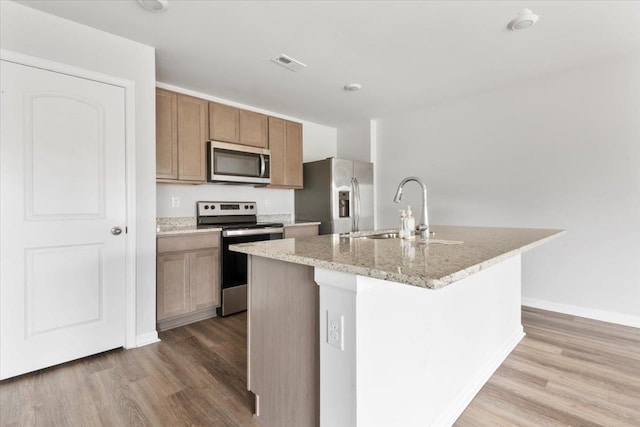  - kitchen featuring appliances with stainless steel finishes, wood finished floors, a center island with sink, and a sink