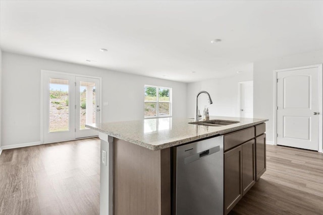  - kitchen featuring dishwasher, a sink, wood finished floors, light stone counters, and a kitchen island with sink