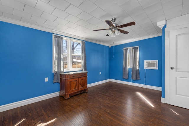 unfurnished bedroom with a wall unit AC, a ceiling fan, baseboards, ornamental molding, and dark wood-type flooring