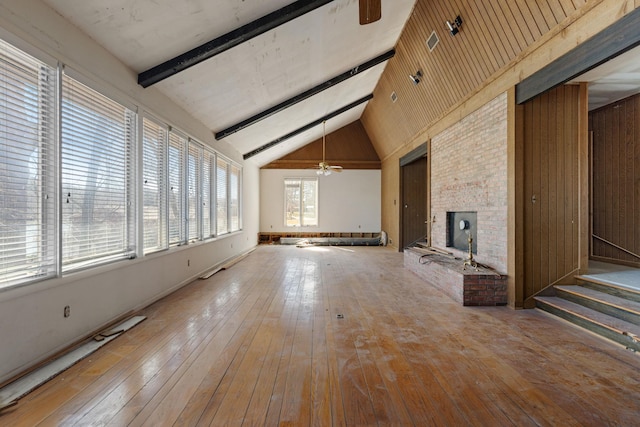 unfurnished living room featuring hardwood / wood-style floors, a brick fireplace, beamed ceiling, and a ceiling fan