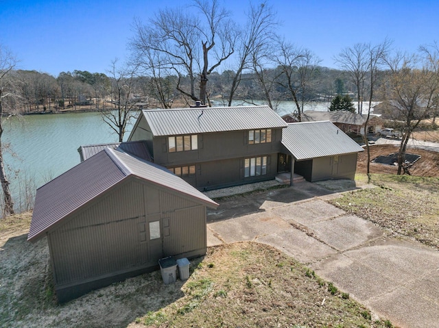 exterior space featuring concrete driveway, metal roof, and a water view