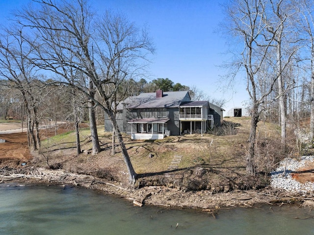 back of property with a water view, a sunroom, and a chimney