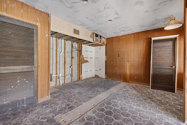 empty room with visible vents, wood walls, and stone finish floor