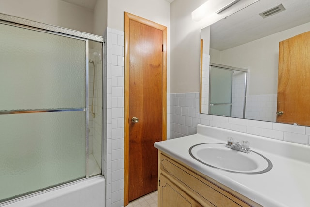 bathroom with vanity, tile walls, and combined bath / shower with glass door