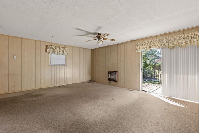 spare room featuring carpet flooring, ceiling fan, a wood stove, and heating unit