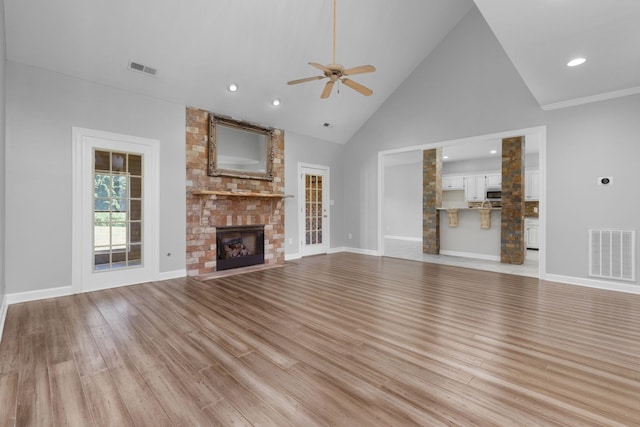 unfurnished living room with ceiling fan, a fireplace, high vaulted ceiling, and light hardwood / wood-style flooring