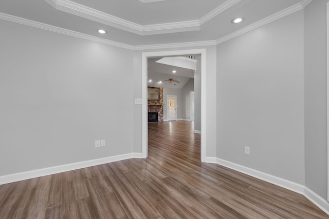 spare room with hardwood / wood-style floors, a raised ceiling, vaulted ceiling, ornamental molding, and a large fireplace