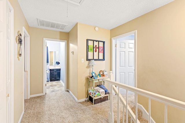  - corridor featuring attic access, light carpet, baseboards, and a textured ceiling