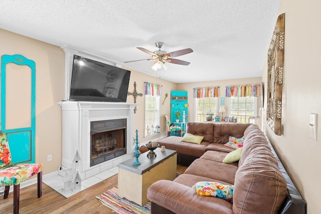 - living area featuring ceiling fan, wood finished floors, a textured ceiling, plenty of natural light, and a fireplace with flush hearth