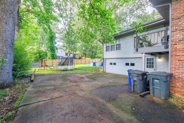  - view of yard with a garage, a playground, a balcony, asphalt driveway, and a trampoline