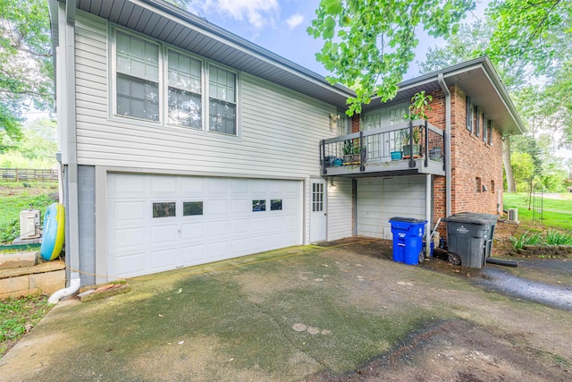  - back of house featuring an attached garage, a balcony, driveway, and brick siding