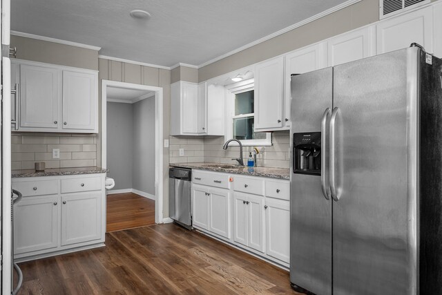 kitchen with appliances with stainless steel finishes, white cabinets, dark wood-style flooring, and ornamental molding