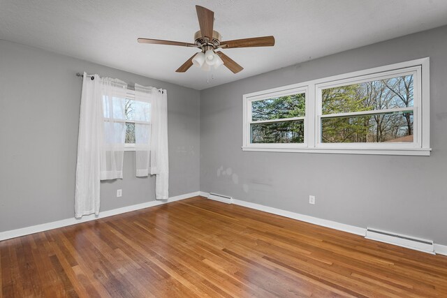 spare room with a baseboard heating unit, wood finished floors, and baseboards