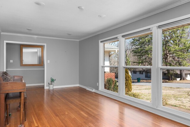 empty room featuring crown molding, baseboards, and wood finished floors