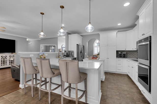  - kitchen featuring stainless steel appliances, ornamental molding, arched walkways, a breakfast bar, and white cabinetry