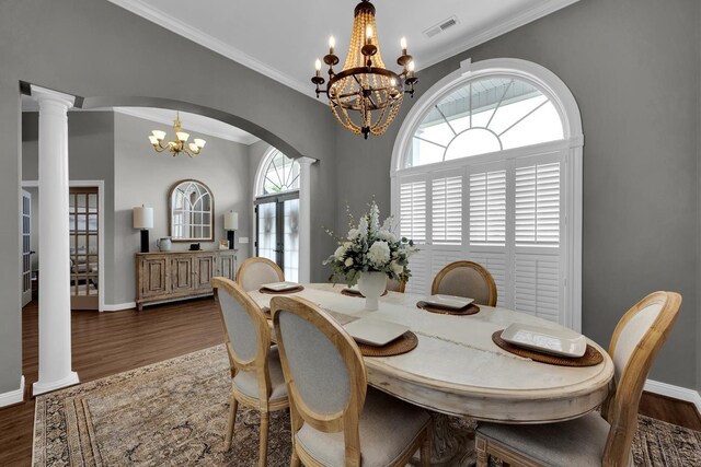  - dining space featuring a chandelier, wood finished floors, crown molding, arched walkways, and ornate columns
