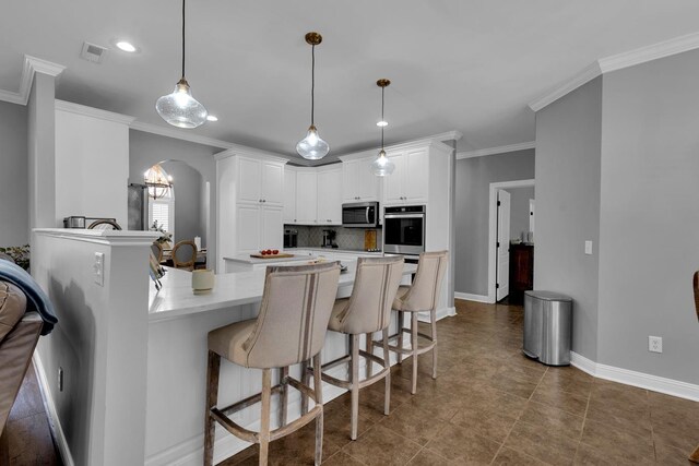  - kitchen with stainless steel microwave, a peninsula, a kitchen bar, ornamental molding, and white cabinetry